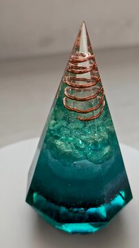 Aquamarine Crystal Orgonite Pyramid with Copper Elements Rotating 360 Degrees on Turntable Over White Marble Background Handmade Epoxy Resin Energy Sculpture Close Up Showcase
