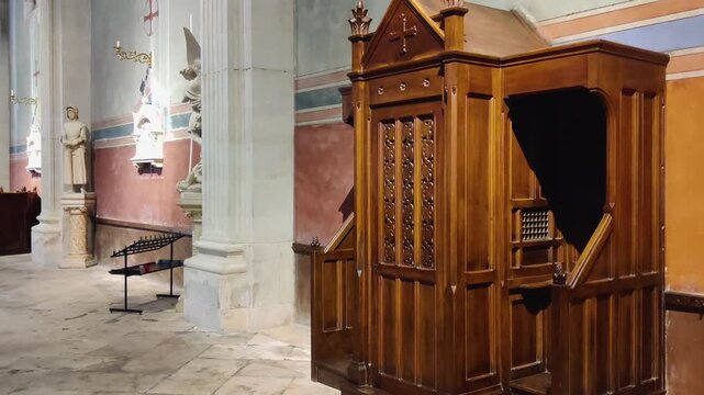 Traditional wooden confessional booth inside historic church interior in France next to holy statues
