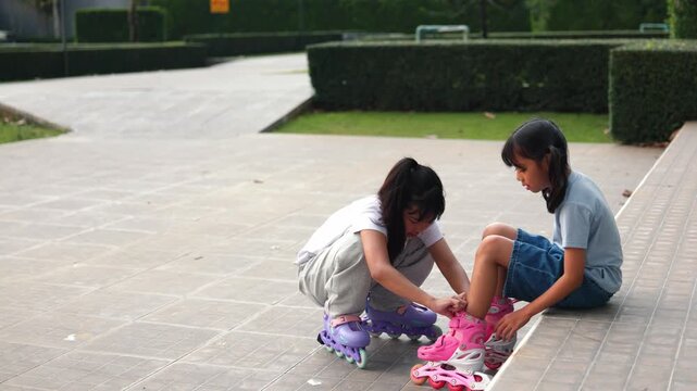 Cute young Asian children girls rollerskating and balancing together inside summer public park green field. Happy classmates enjoying joyful outdoor exercise scene process.
