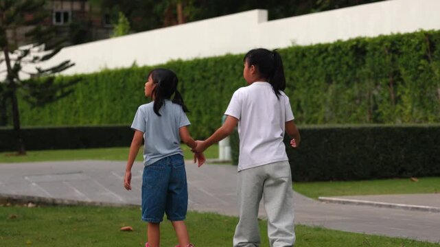 Happy Asian children girls exercising balance and rollerskating together inside public park meadow. Cute young friends playing joyful sport hobby lifestyle session project.