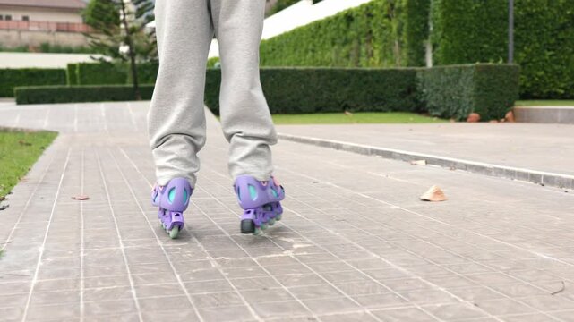 Two active elementary Asian girls teaching rollerskate sport hobby to companion inside public park track. Happy child friends enjoying recreation fitness training match session.