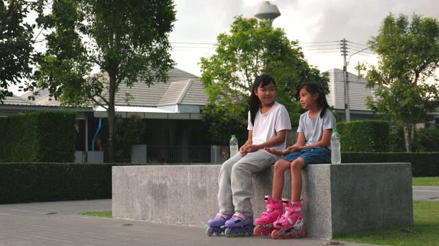 Cute young Asian children girls rollerskating and balancing together inside summer public park green field. Happy classmates enjoying joyful outdoor exercise routine process.
