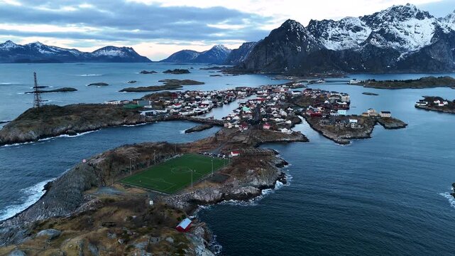 Scenic Drone Flyover of Henningsvaer Soccer Field Encircled by Arctic Ocean and Snowy Mountains, Lofoten Norway at blue hour, horizontal drone shot