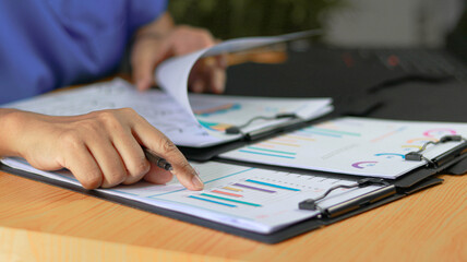 Healthcare professional reviewing analytical reports and performance charts on documents, supporting medical administration, healthcare data analysis, strategic planning, and operational decision © Siwaporn