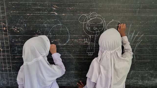 Creative Muslim Elementary School Student Drawing with Chalk on Blackboard in Classroom