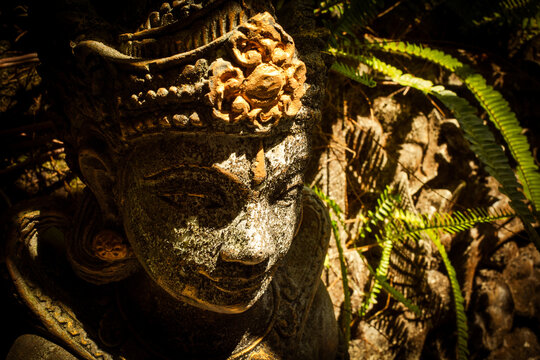 Balinese stone statue of Dewi Sri, the goddess of rice and prosperity, offering spiritual symbolism and cultural heritage in a lush tropical garden environment in Bali, Indonesia