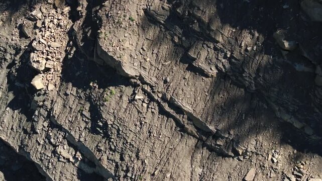 Exposed rock layers and loose rubble on the steep wall of an active quarry. The excavated slope reveals geological strata, fractured stone, and raw mineral deposits in an industrial extraction site.