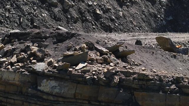 Exposed rock layers and loose rubble on the steep wall of an active quarry. The excavated slope reveals geological strata, fractured stone, and raw mineral deposits in an industrial extraction site.