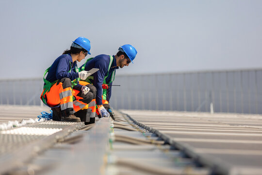 Workers installing solar panels on rooftop, Solar energy technicians inspecting photovoltaic modules on industrial roof, Professional team maintaining solar panel system for sustainable