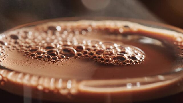 Close-up of frothy hot chocolate with steam rising in a clear glass mug