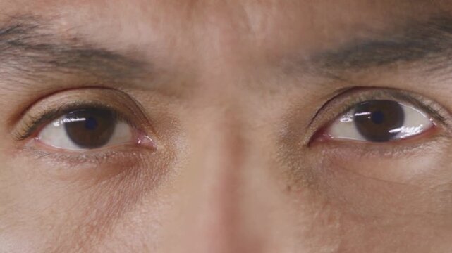 A close up shot of a young asian man with dark brown eyes opening his eyes and looking into the camera in slow motion.