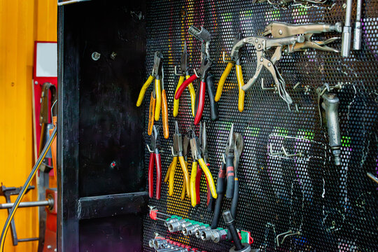 Professional pegboard tool wall in a mechanic's workshop, various pliers, locking pliers, assorted hand tools. Authentic  precision automotive repair, industrial maintenance, skilled mechanical work.