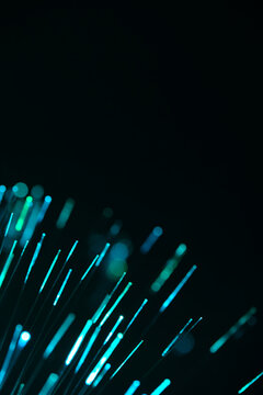 Vibrant turquoise fiber optic lines flare up diagonally from corner against black backdrop.