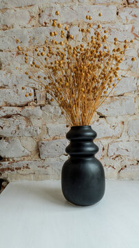 Dried flax seed pods in a black vase against a textured brick wall