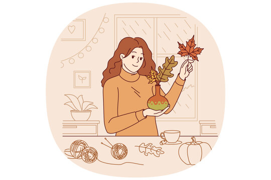 Woman collects bouquet of autumn leaves and places them in vase to decorate home on thanksgiving eve. Girl rejoices at arrival of autumn and makes decorations for apartment, creating cozy atmosphere
