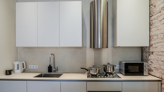 Modern kitchen interior with white cabinets, stainless steel appliances, and brick wall accent