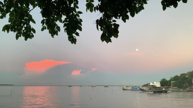 4K sunset seascape with fishing boats and glowing clouds at Tanjung Lesung Beach, Banten, Indonesia. Gentle shoreline waves create a peaceful ambiance, ideal for travel and relaxation themes.