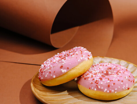 Fresh donuts on a plate with pink icing and sprinkles in a simple setting