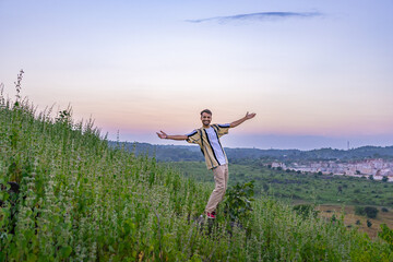 Fototapeta premium Man standing on grassy hill with arms outstretched, enjoying scenic landscape at sunset, Banswara, Udaipur, Rajasthan