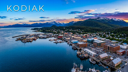 Naklejka premium The scenic coastal town of Kodiak at sunset, featuring a busy harbor filled with boats and mountains in the background