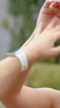 Vertical video: High-fiving greeting woman showing French nails in garden, white watch, copy space
