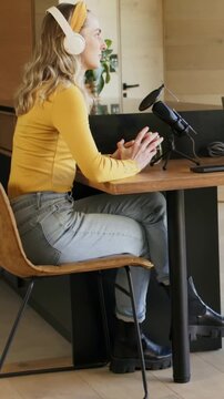 Vertical video: Starting host wearing yellow top and headset speaking at home into mic, holding cup