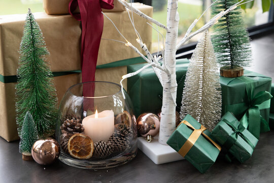 Holiday display sitting on dark tabletop by window with glass bowl with lit pillar candle, gifts