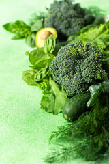 A variety of fresh green vegetables and herbs are arranged neatly on a bright green surface. Among them are cucumbers, broccoli, leafy greens, avocado, and basil, perfect for healthy cooking or salads © pundapanda