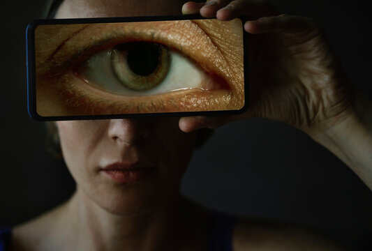 Woman indoors holding smartphone with large eye over her face