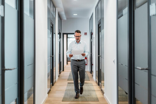 Businessman checking document while walking at office corridor