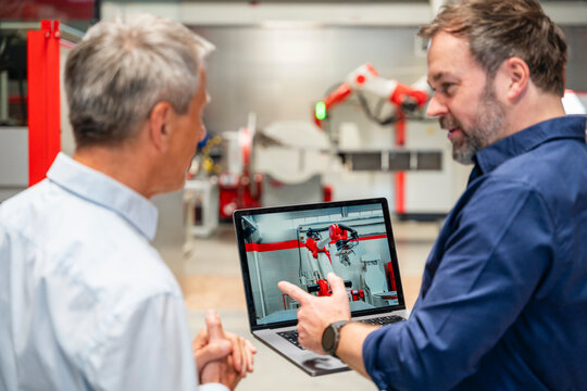 Employees discussing industrial robot on laptop in factory