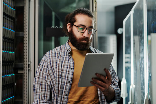 Technician wearing eyeglasses looking at tablet PC in server room