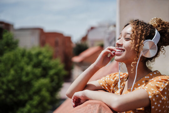 Happy woman with eyes closed listening music in balcony
