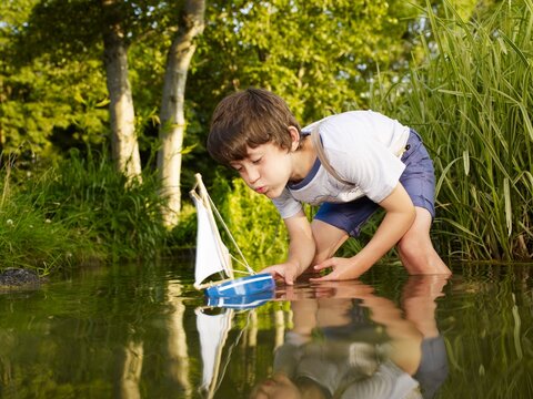 Child playing with a toy sailing boat in a summer stream