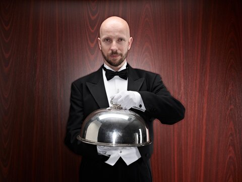 Butler in tuxedo presenting a silver tray with cloche