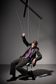 Businessman sitting in office chair manipulated like a puppet