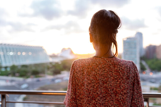 Woman standing in balcony while looking at sunset