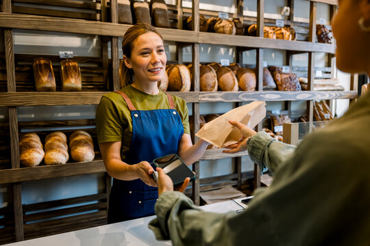 Bakery owner accepting mobile phone payment from client at counter
