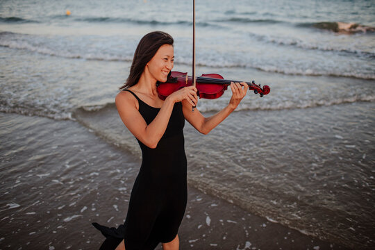 Happy woman playing violin in sea at beach