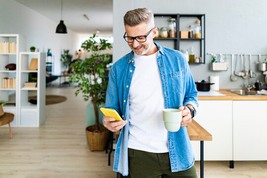Man holding coffee cup while using smart phone in kitchen