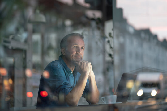 Businessman sitting at table with hand on chin looking through window