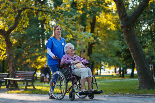 Smiling healthcare worker walking with senior woman sitting in wheelchair at park