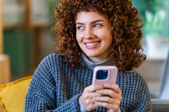 Smiling womanwith curly hair using a smartphone at home