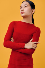 Obraz premium Young woman in red long sleeve sweater stands with crossed arms looking confident and thoughtful against orange background. Fashion portrait with casual style and minimalistic colors.