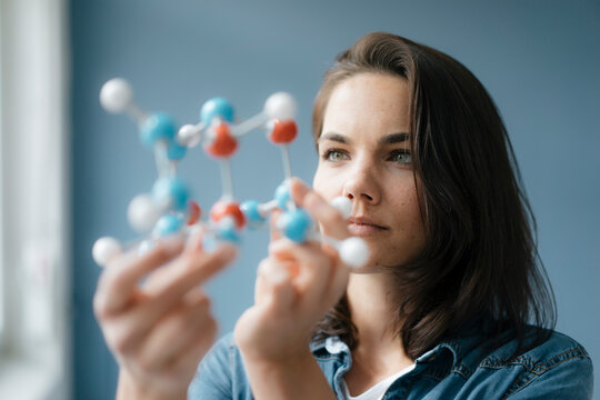 Female scientist studying molecule model, looking for solutions