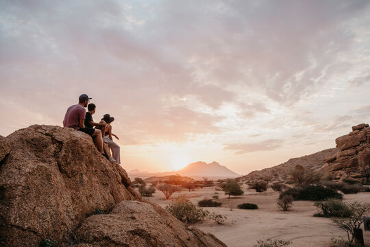 Namibia, Spitzkoppe, friends sitting on a rock watching the sunset
