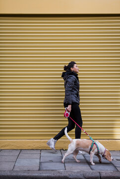 Woman and her dog walking on pavement in front of a roller shutter