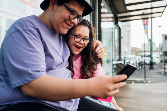 Smiling brother sharing smart phone with sister at bus station