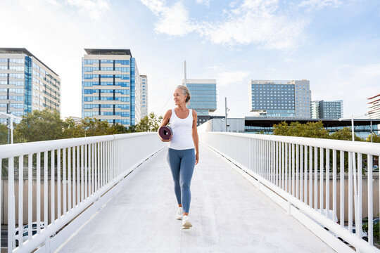 Woman holding exercise mat walking on footbridge