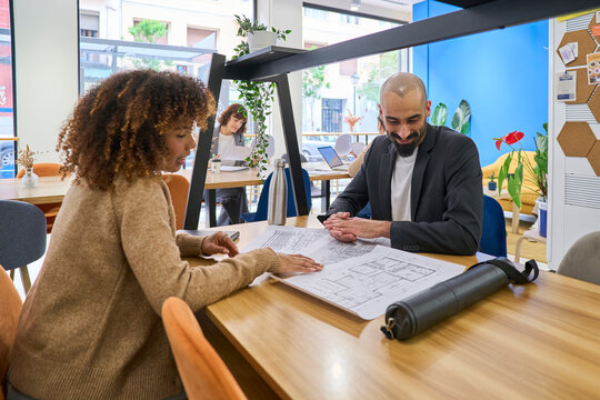 Architect and client analyzing a blueprint in an office